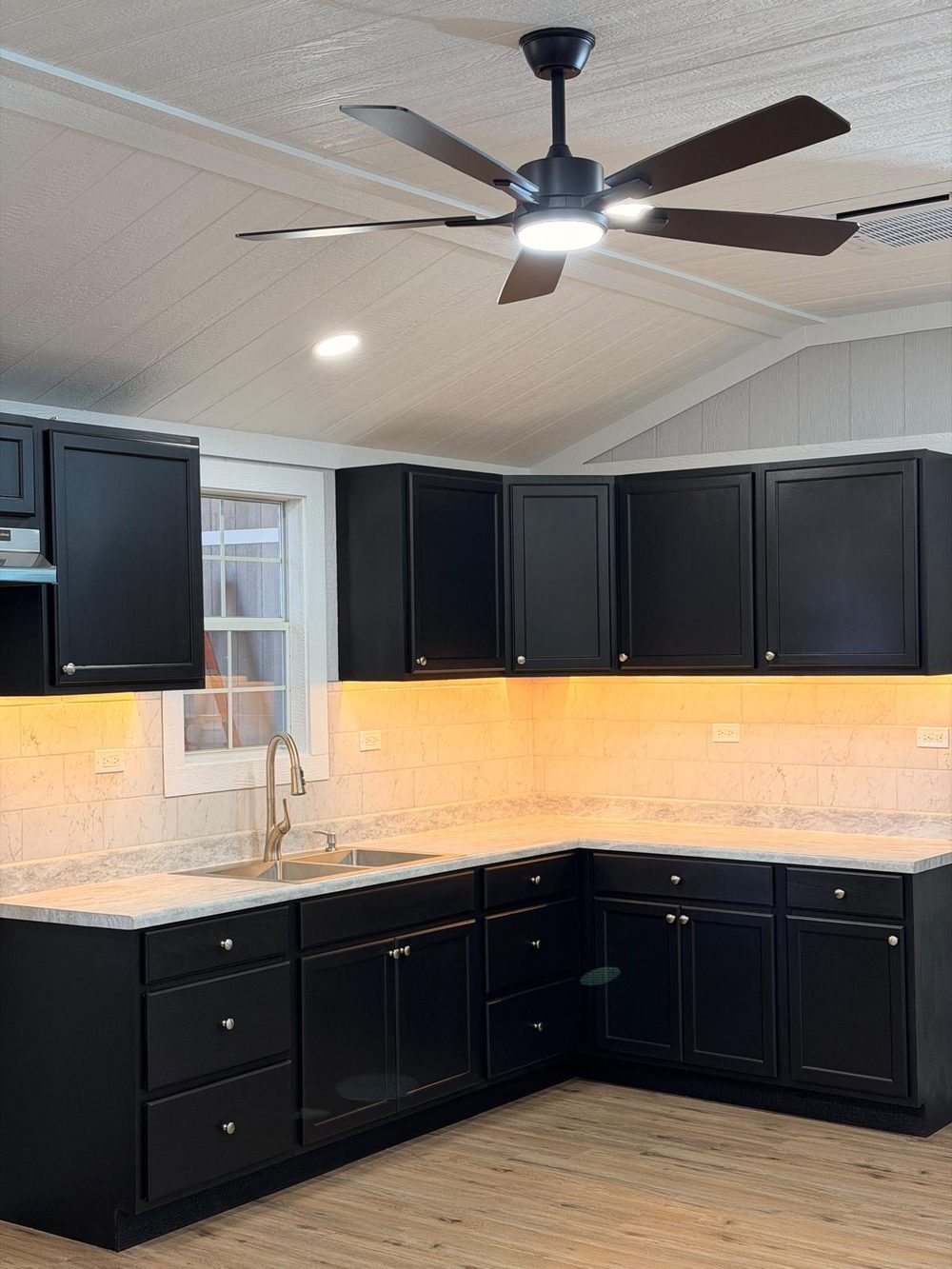 L-shaped kitchen with black cabinets, marble-look counters and tile backsplash